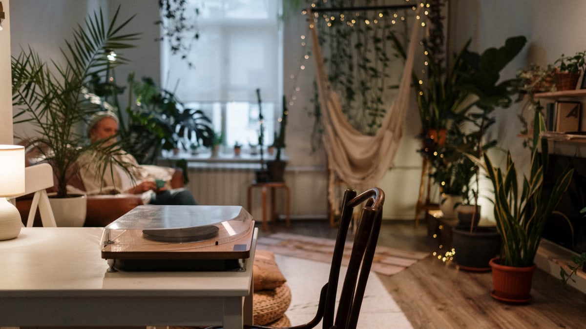 A cozy living room with plants, a hammock, and a vintage turntable, perfect for relaxation.